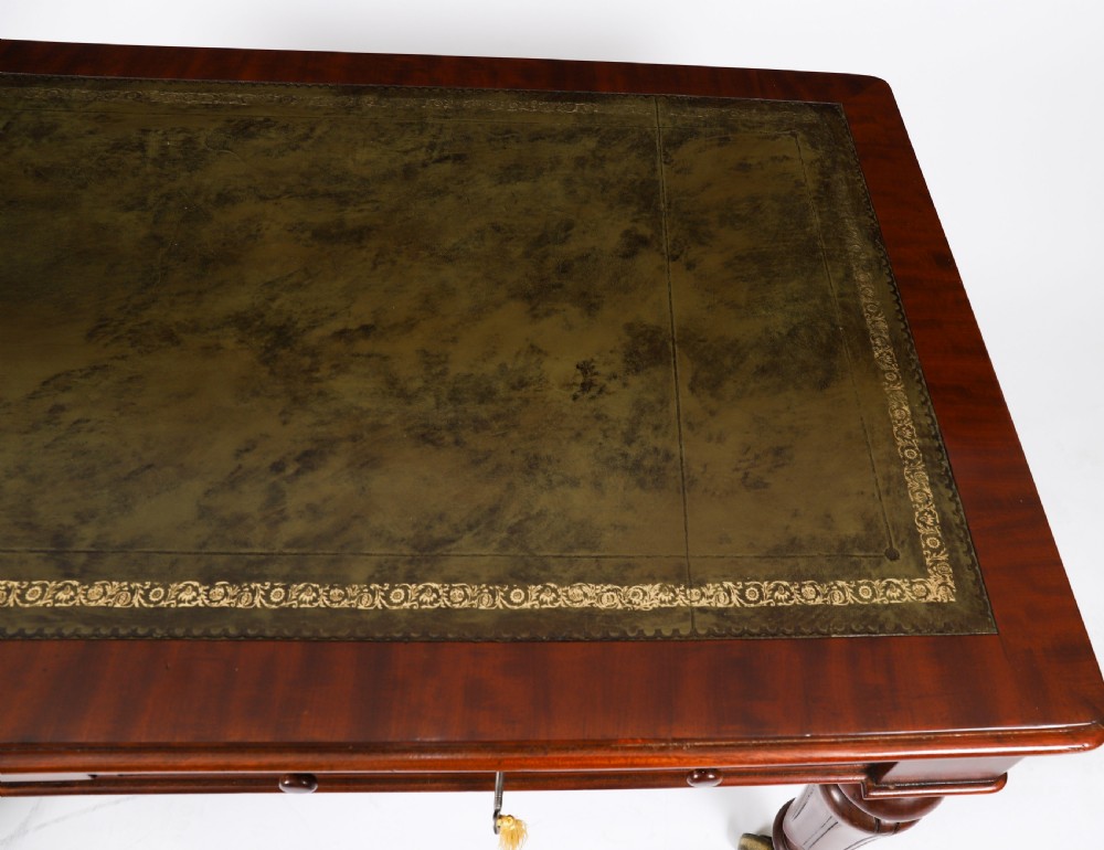 A William IV mahogany writing desk featuring an inset green leather surface, two frieze drawers with knob handles, turned fluted legs, and brass castors. View V