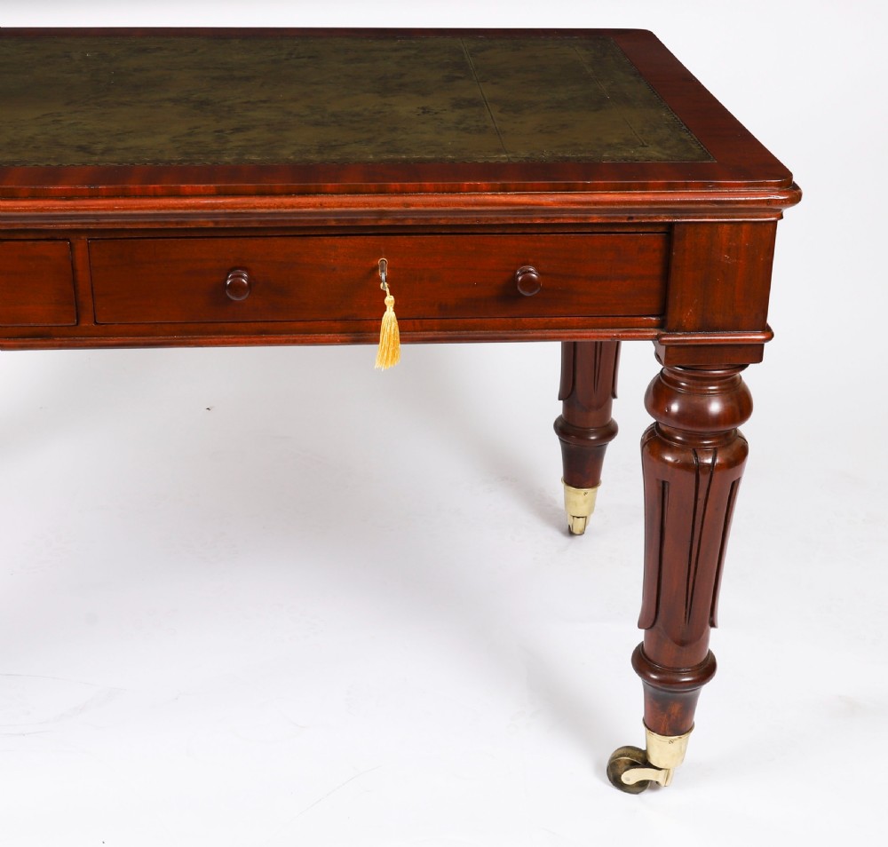 A William IV mahogany writing desk featuring an inset green leather surface, two frieze drawers with knob handles, turned fluted legs, and brass castors. View XI