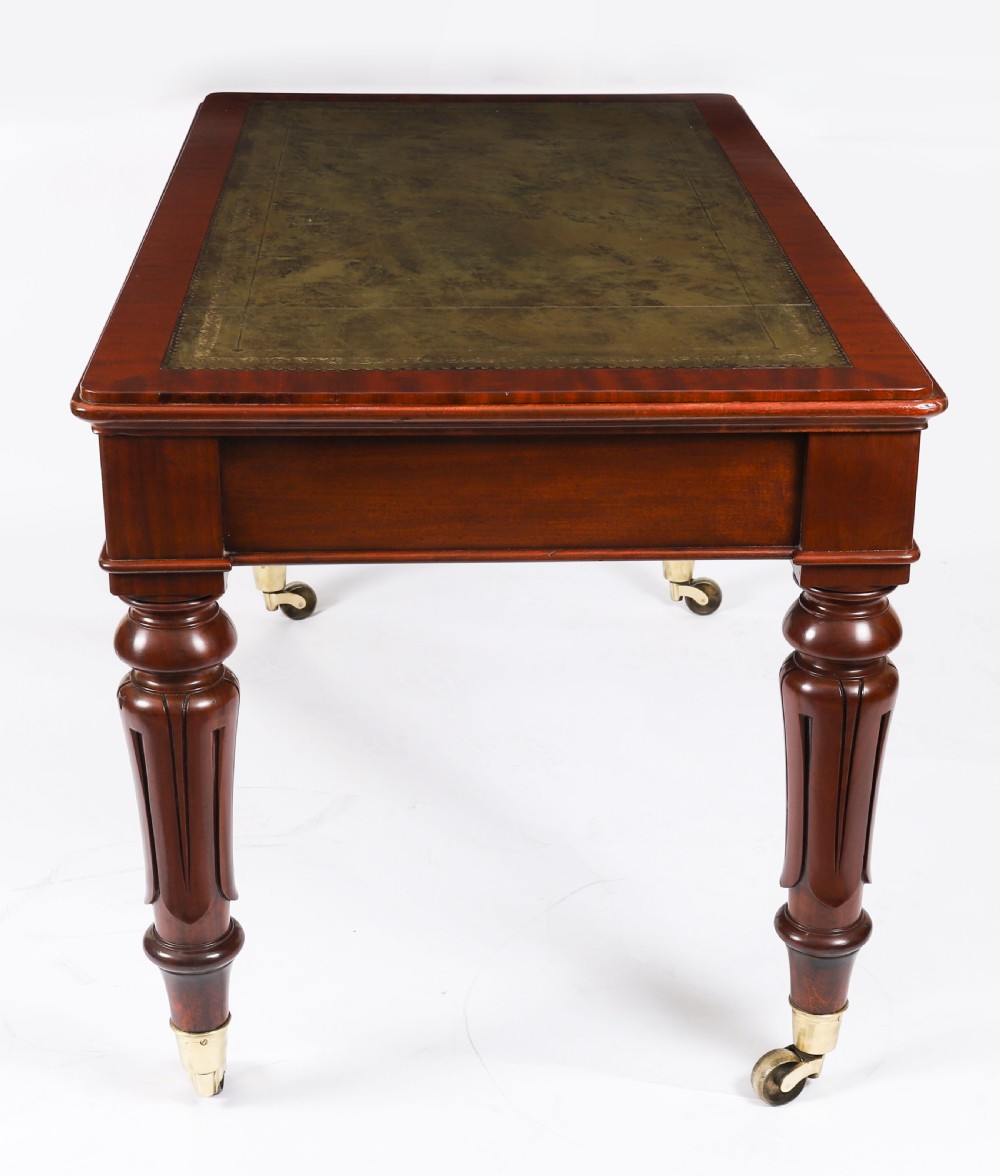 A William IV mahogany writing desk featuring an inset green leather surface, two frieze drawers with knob handles, turned fluted legs, and brass castors. View XII