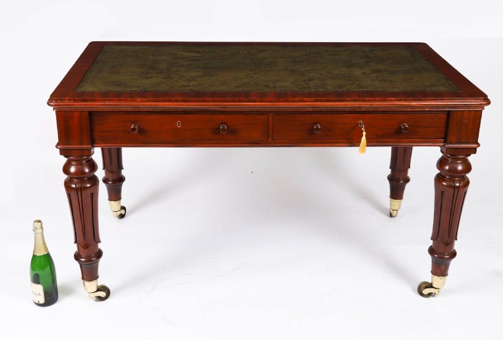A William IV mahogany writing desk featuring an inset green leather surface, two frieze drawers with knob handles, turned fluted legs, and brass castors. View XIII