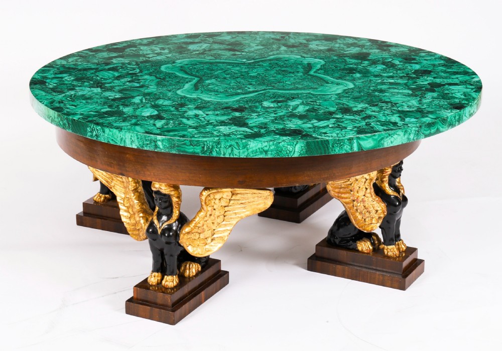 A round coffee table featuring a green malachite stone veneer top supported by three carved ebonised and giltwood winged sphinx legs on dark plinth bases. View II