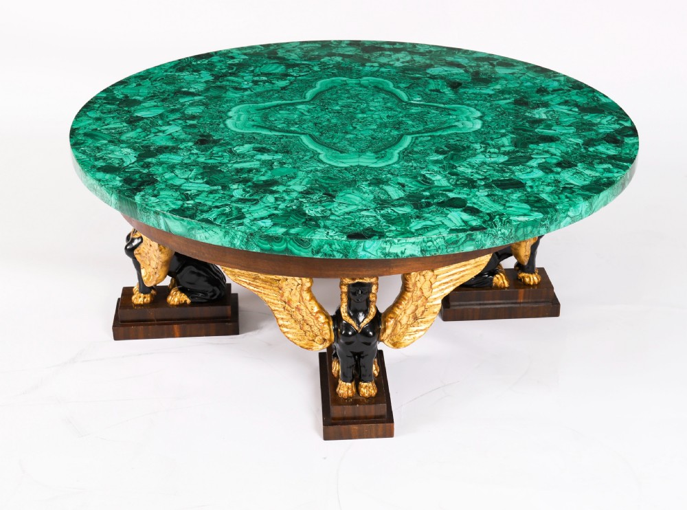 A round coffee table featuring a green malachite stone veneer top supported by three carved ebonised and giltwood winged sphinx legs on dark plinth bases. View IV