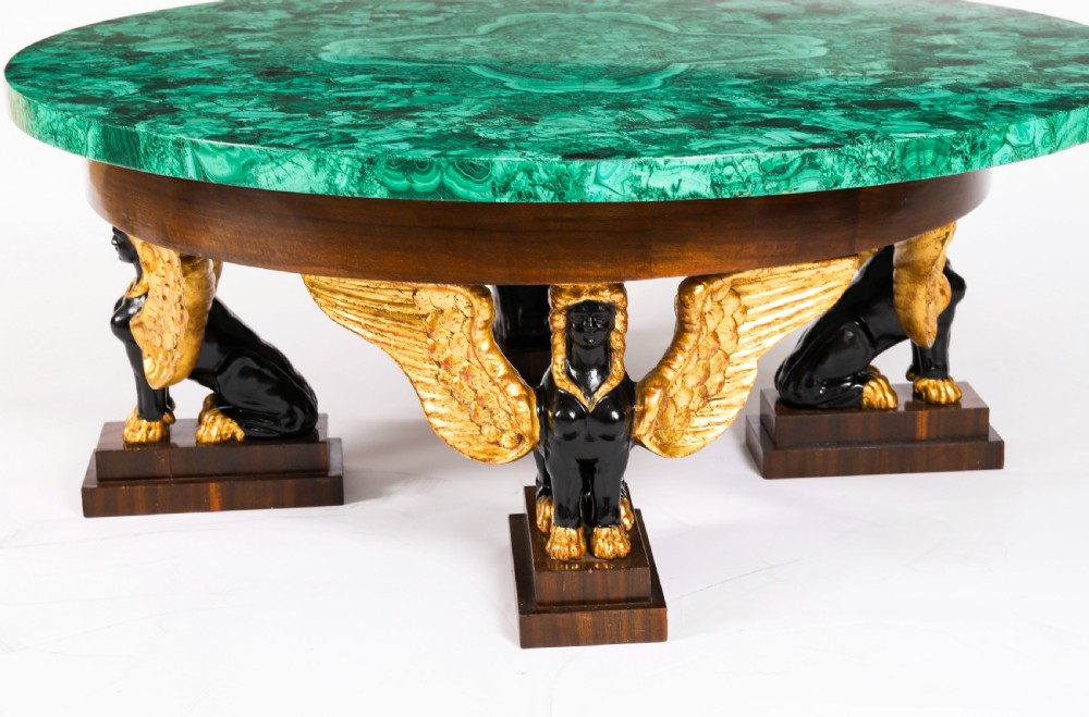 A round coffee table featuring a green malachite stone veneer top supported by three carved ebonised and giltwood winged sphinx legs on dark plinth bases. View VI