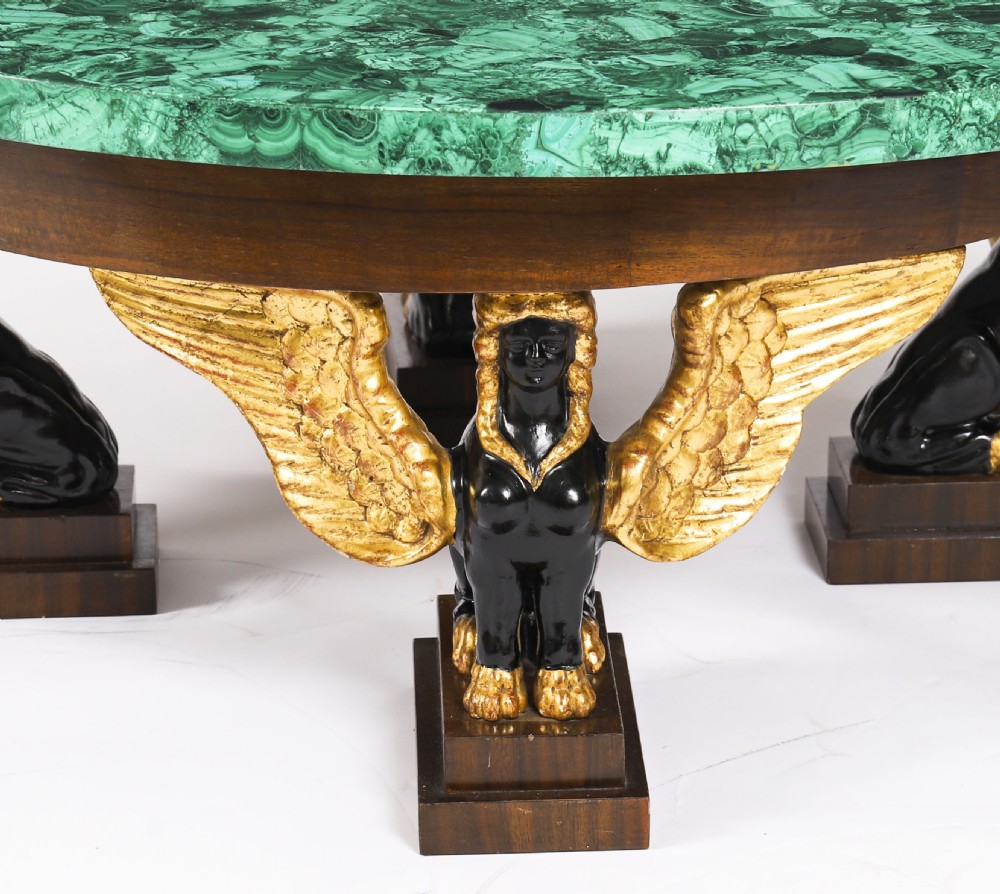 A round coffee table featuring a green malachite stone veneer top supported by three carved ebonised and giltwood winged sphinx legs on dark plinth bases. View VII
