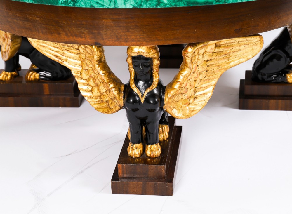 A round coffee table featuring a green malachite stone veneer top supported by three carved ebonised and giltwood winged sphinx legs on dark plinth bases. View XIV