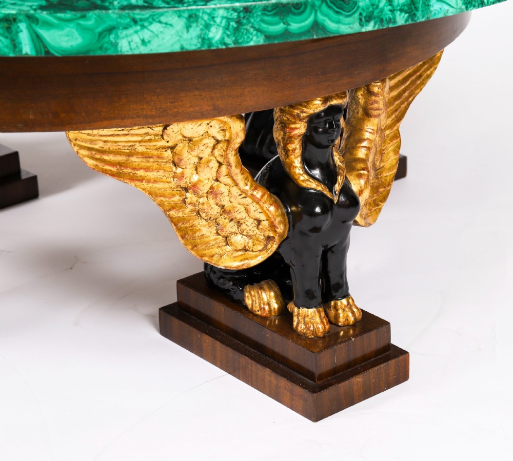 A round coffee table featuring a green malachite stone veneer top supported by three carved ebonised and giltwood winged sphinx legs on dark plinth bases. View XV