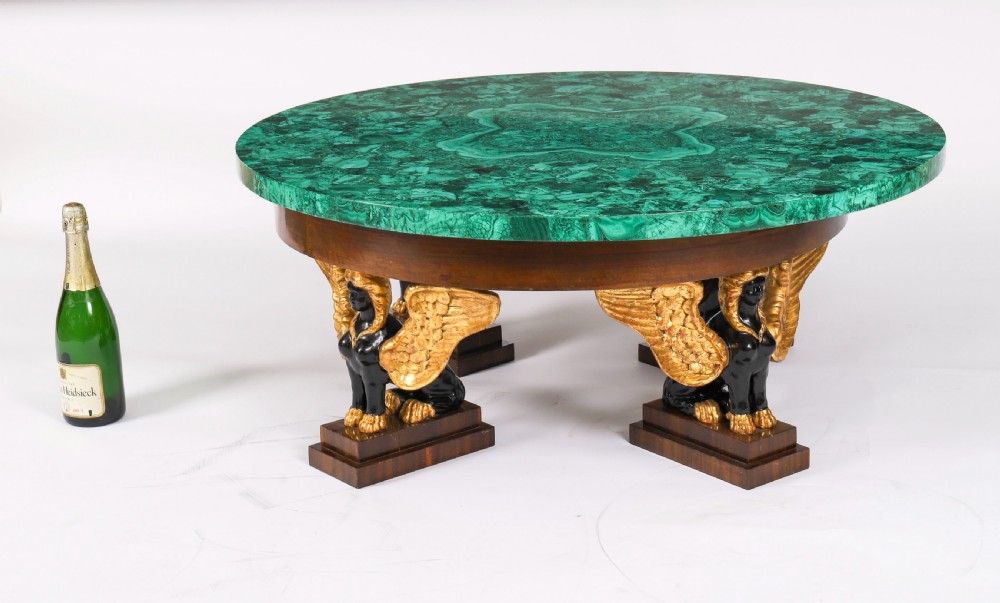 A round coffee table featuring a green malachite stone veneer top supported by three carved ebonised and giltwood winged sphinx legs on dark plinth bases. View XVII