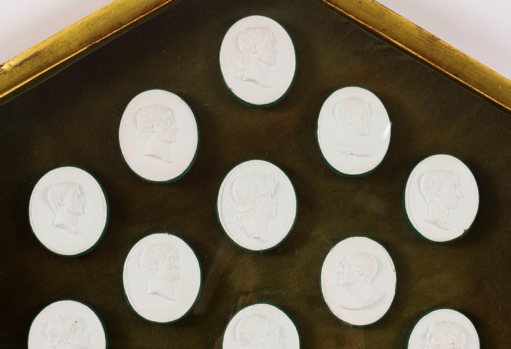 A hexagonal giltwood frame housing thirteen classical white plaster profile intaglios mounted against a dark green background. View II