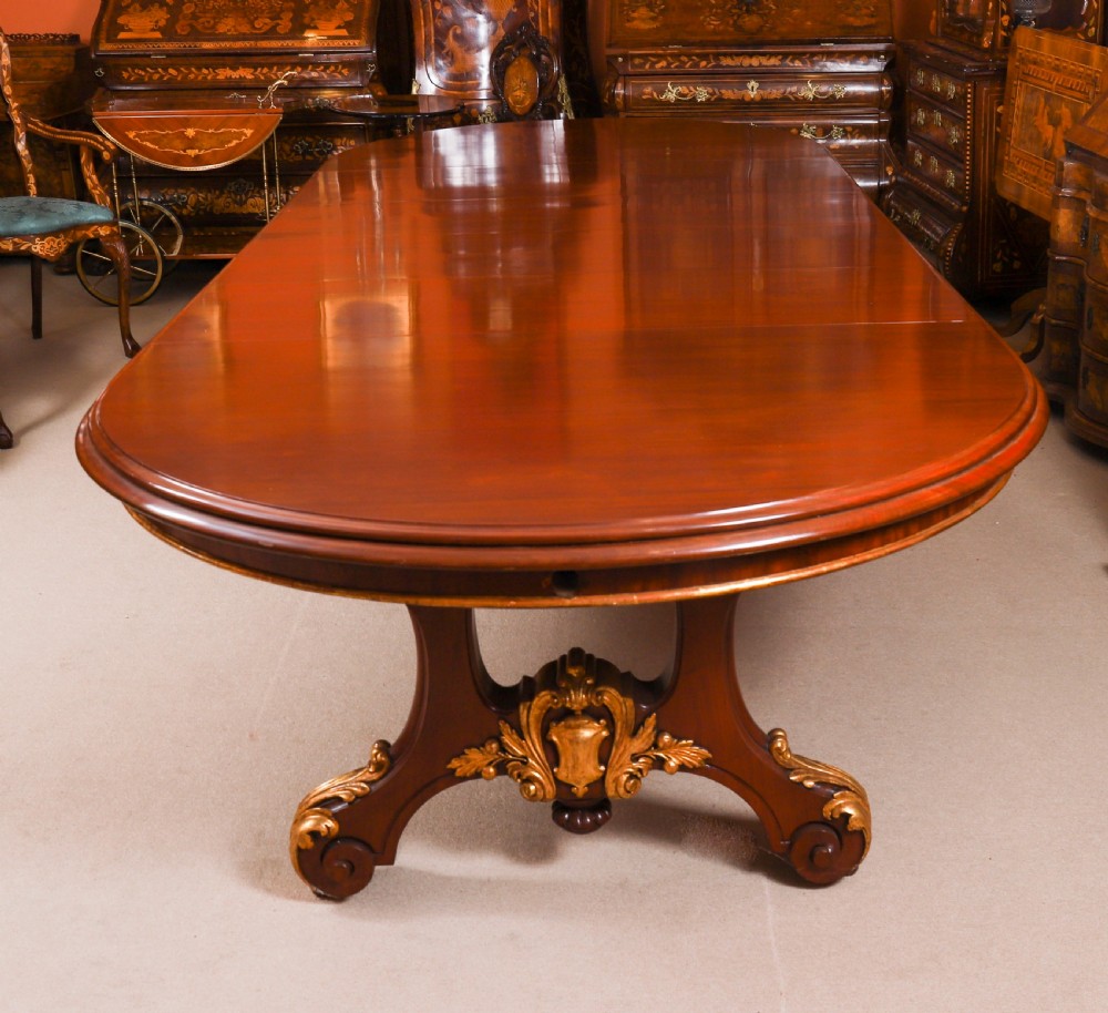 A large, polished mahogany extending dining table supported by two carved twin pedestals with parcel-gilt detailing. View V