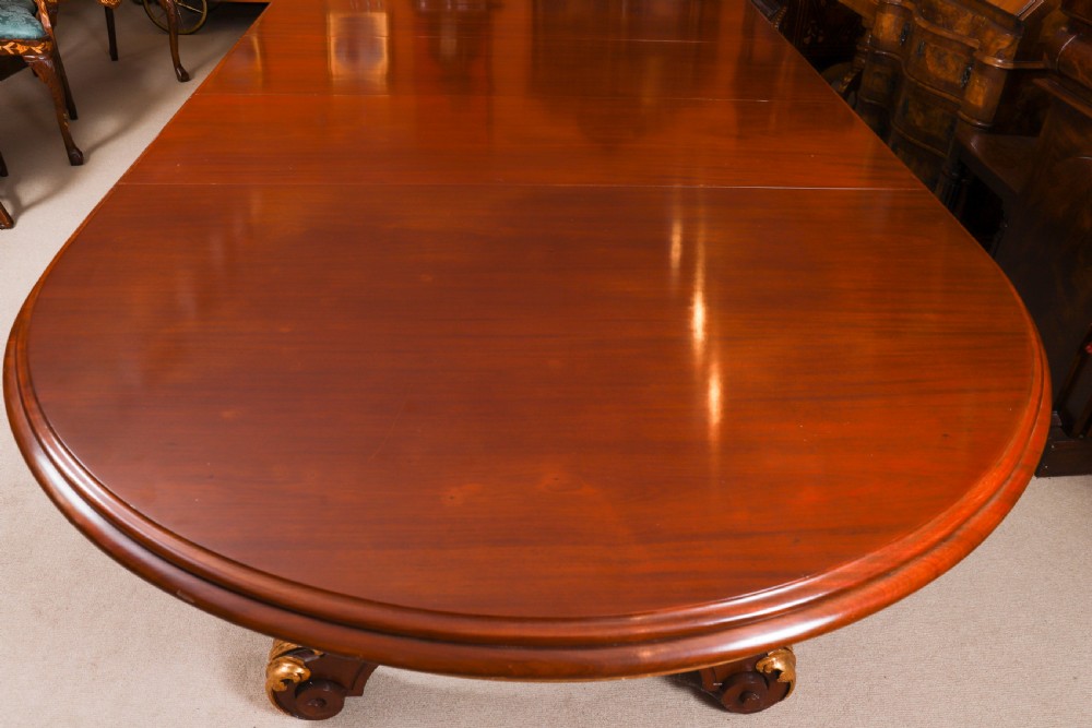 A large, polished mahogany extending dining table supported by two carved twin pedestals with parcel-gilt detailing. View VII