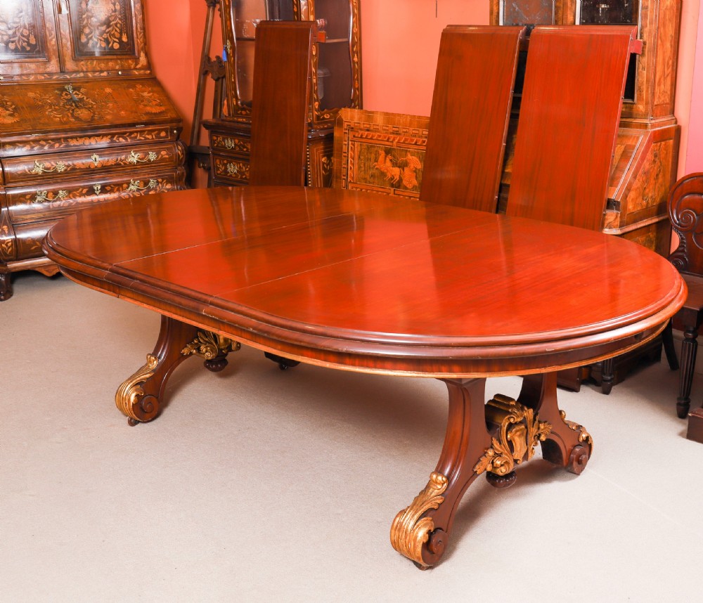 A large, polished mahogany extending dining table supported by two carved twin pedestals with parcel-gilt detailing. View XII