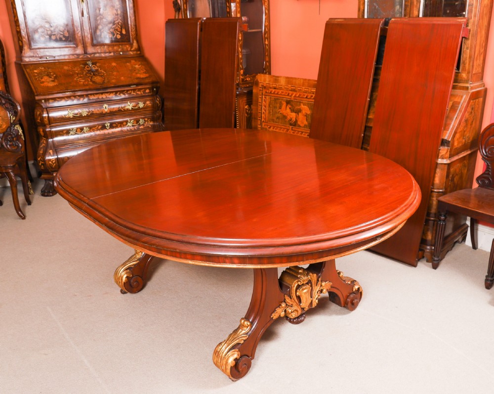 A large, polished mahogany extending dining table supported by two carved twin pedestals with parcel-gilt detailing. View XIII