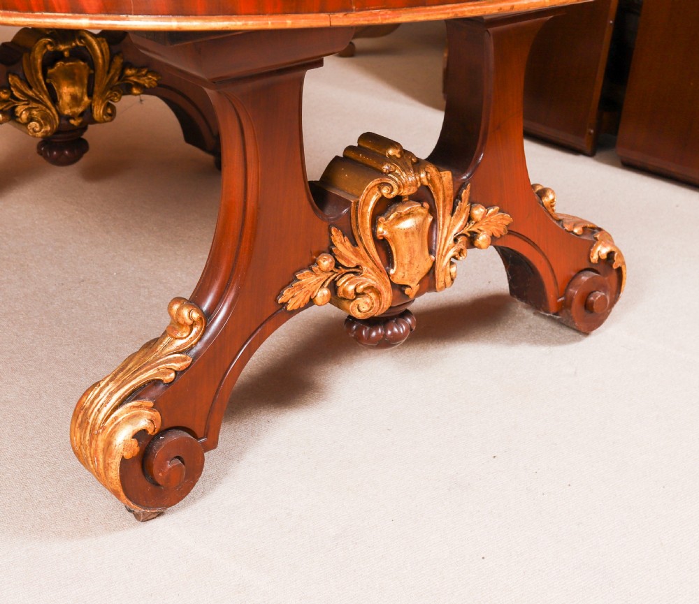 A large, polished mahogany extending dining table supported by two carved twin pedestals with parcel-gilt detailing. View XVI
