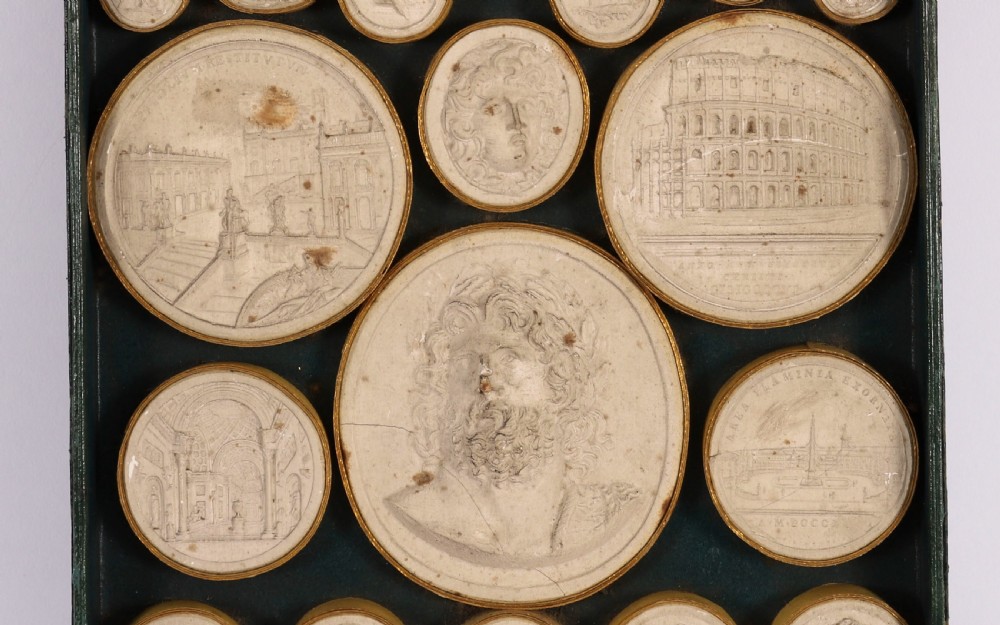 An 18th-century boxed set of cream plaster Grand Tour intaglios showing classical profile portraits and Roman architectural scenes alongside an Italian manuscript index. View V