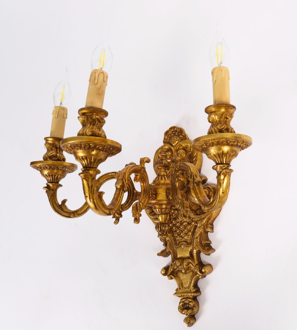 A set of four French Rococo style gilt bronze wall lights, each featuring three scrolling arms adorned with acanthus leaf motifs and candle drip sockets. View XIV