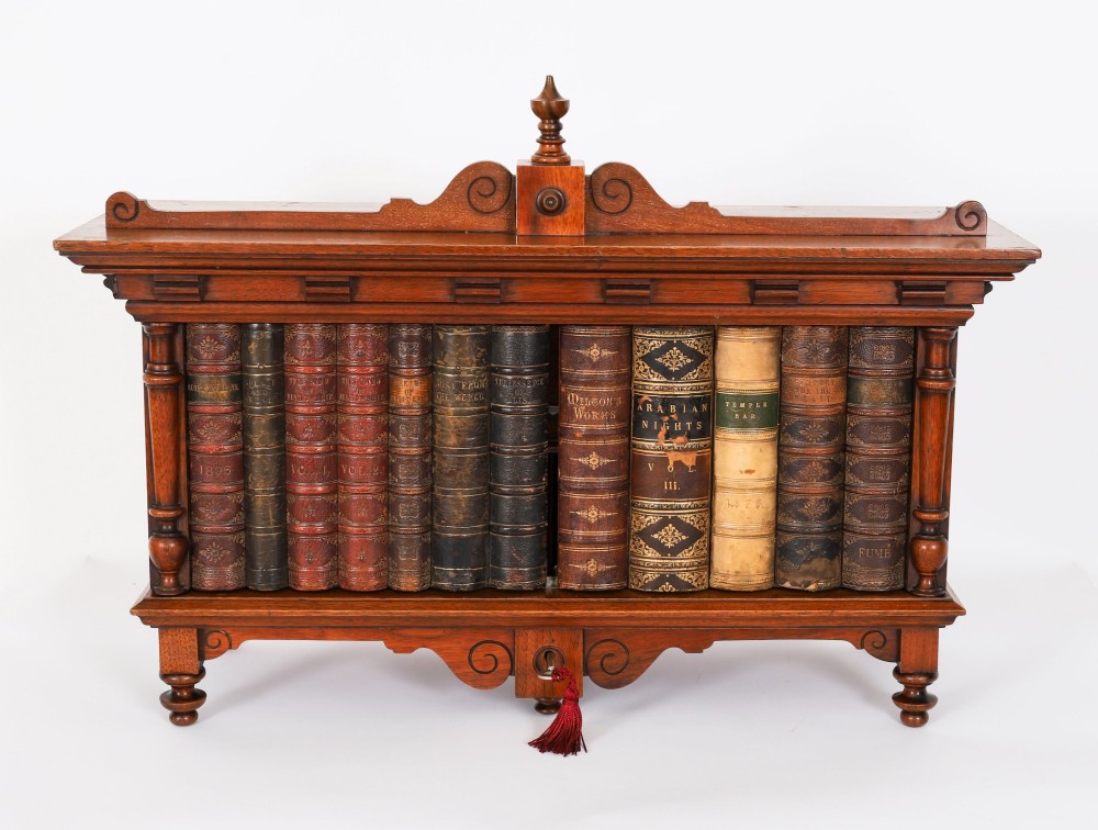 An antique Victorian walnut tabletop collectors cabinet featuring a front styled with vintage book spines, turned columns, turned feet, and a central finial top. View II