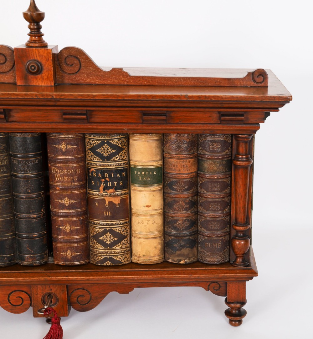 An antique Victorian walnut tabletop collectors cabinet featuring a front styled with vintage book spines, turned columns, turned feet, and a central finial top. View VI
