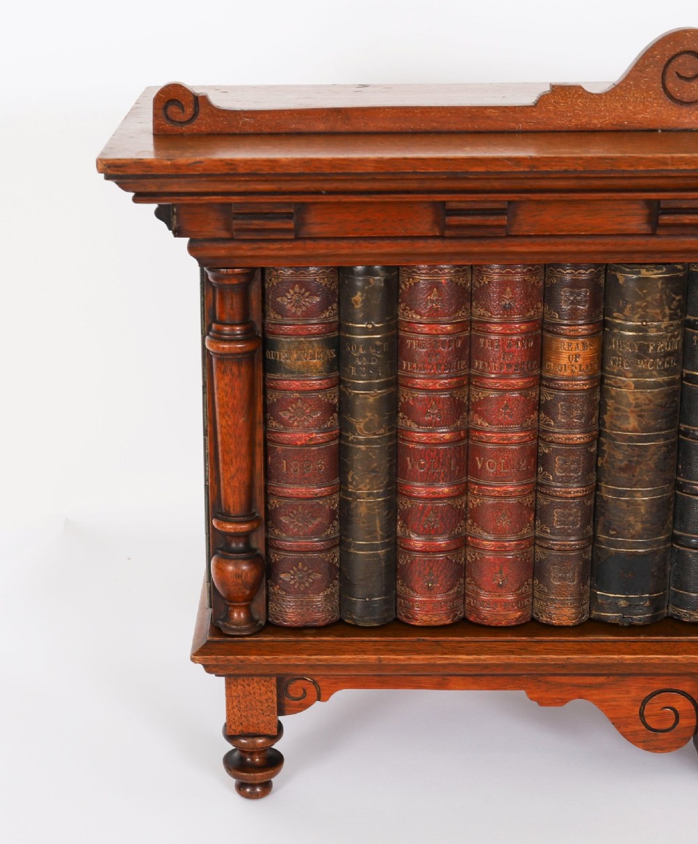 An antique Victorian walnut tabletop collectors cabinet featuring a front styled with vintage book spines, turned columns, turned feet, and a central finial top. View VII