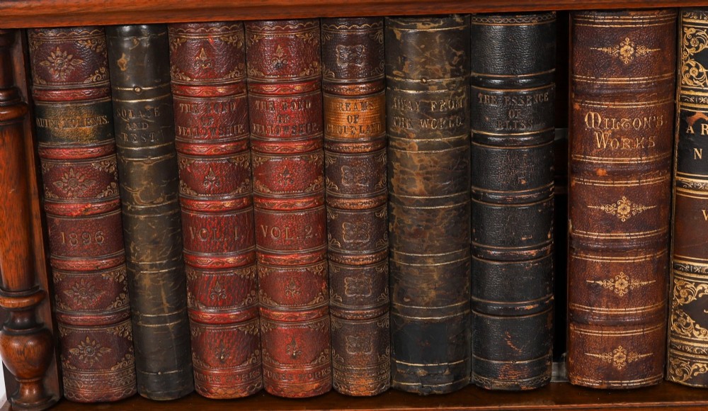 An antique Victorian walnut tabletop collectors cabinet featuring a front styled with vintage book spines, turned columns, turned feet, and a central finial top. View VIII