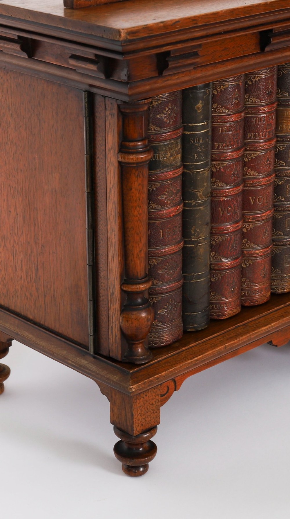 An antique Victorian walnut tabletop collectors cabinet featuring a front styled with vintage book spines, turned columns, turned feet, and a central finial top. View XV