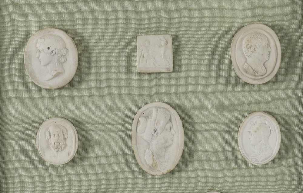 A pair of framed displays containing white plaster intaglio relief medallions mounted on green patterned fabric inside gilt frames. View V