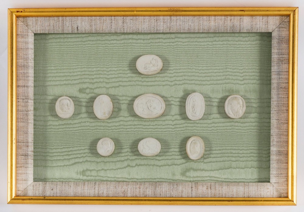 A pair of framed displays containing white plaster intaglio relief medallions mounted on green patterned fabric inside gilt frames. View VIII