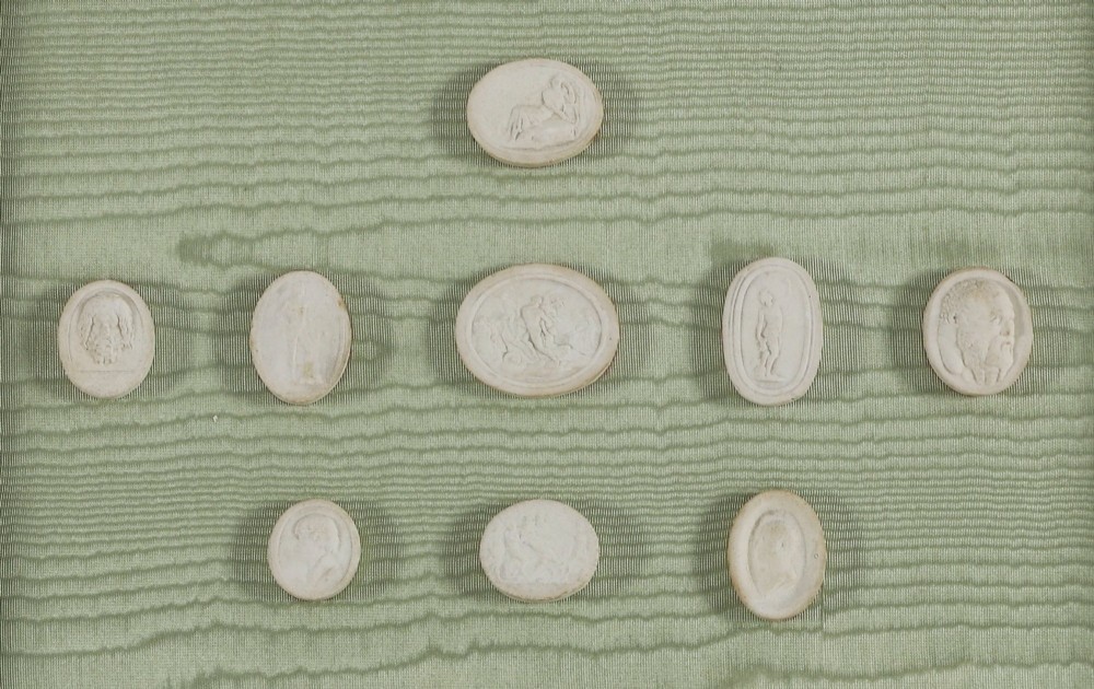 A pair of framed displays containing white plaster intaglio relief medallions mounted on green patterned fabric inside gilt frames. View IX
