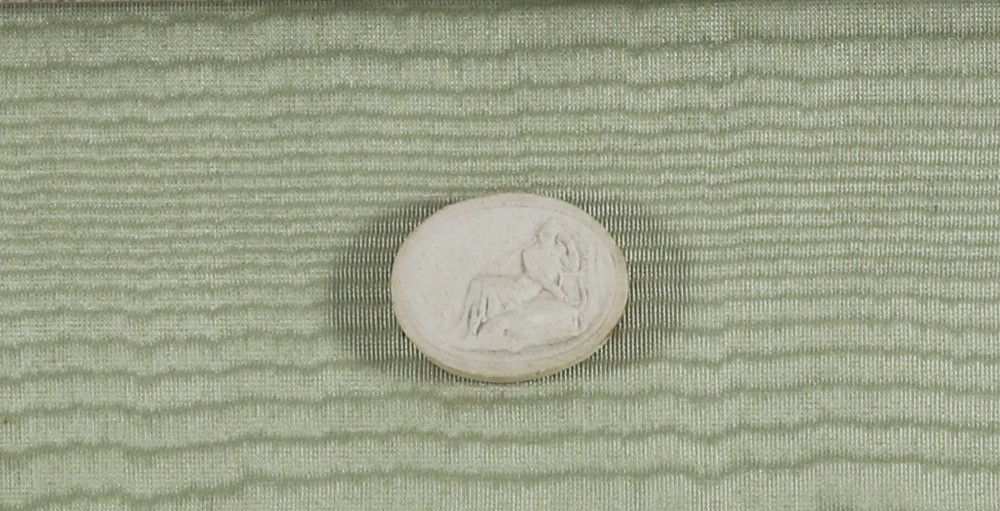 A pair of framed displays containing white plaster intaglio relief medallions mounted on green patterned fabric inside gilt frames. View X