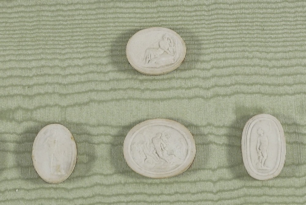 A pair of framed displays containing white plaster intaglio relief medallions mounted on green patterned fabric inside gilt frames. View XI