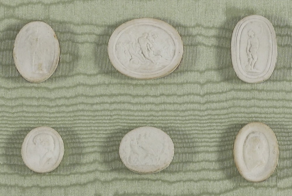 A pair of framed displays containing white plaster intaglio relief medallions mounted on green patterned fabric inside gilt frames. View XII