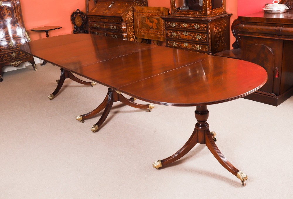 An extended mahogany Regency Revival triple pillar dining table with reeded legs and brass paw castors.