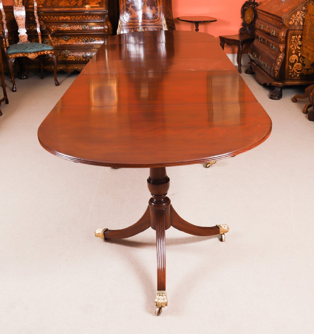 An extended mahogany Regency Revival triple pillar dining table with reeded legs and brass paw castors. View II