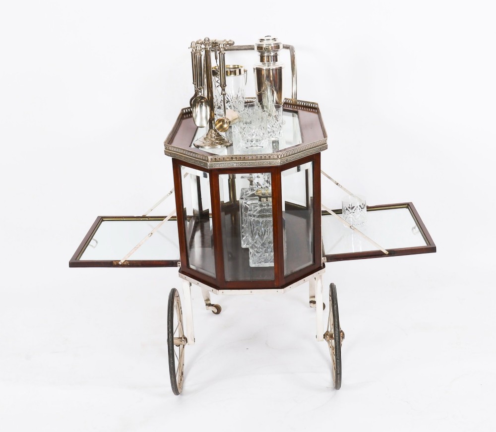 An Art Deco drinks trolley featuring an octagonal glass top with metal gallery trim, wooden side frames, spoked wheels, and a drop-down door. View V