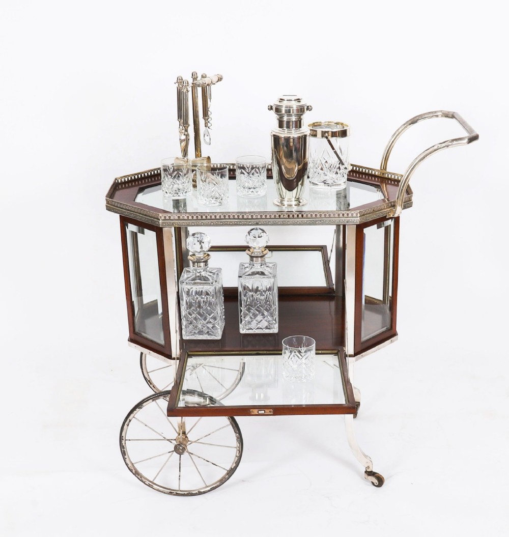 An Art Deco drinks trolley featuring an octagonal glass top with metal gallery trim, wooden side frames, spoked wheels, and a drop-down door. View VI