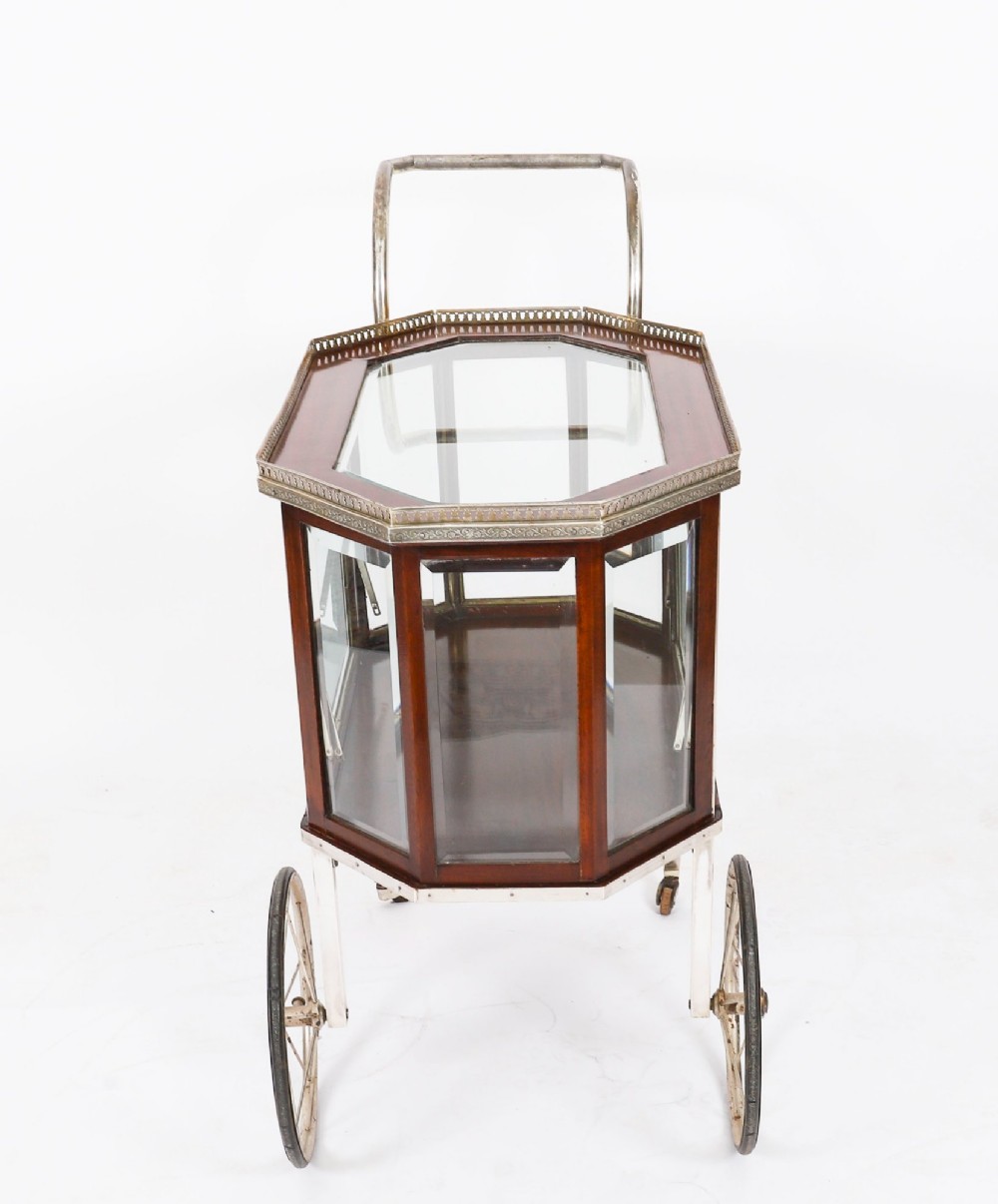 An Art Deco drinks trolley featuring an octagonal glass top with metal gallery trim, wooden side frames, spoked wheels, and a drop-down door. View VIII