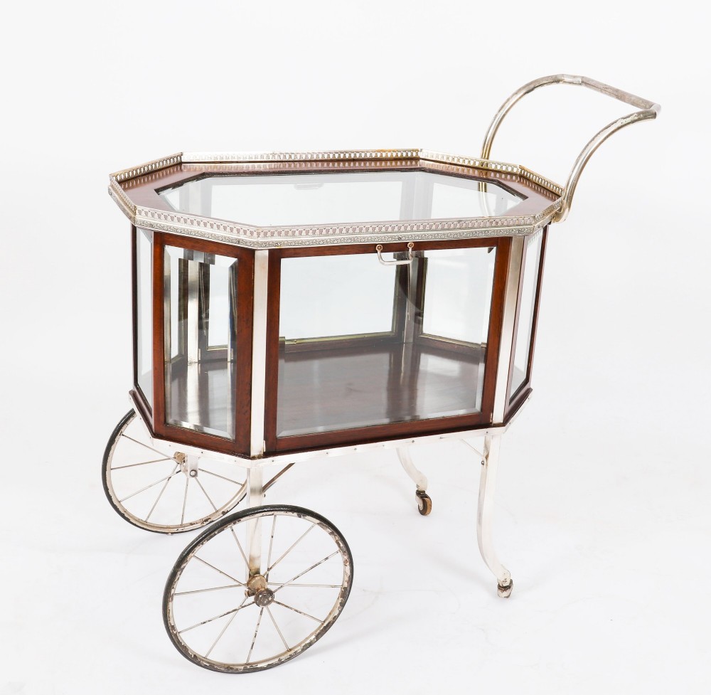 An Art Deco drinks trolley featuring an octagonal glass top with metal gallery trim, wooden side frames, spoked wheels, and a drop-down door. View IX