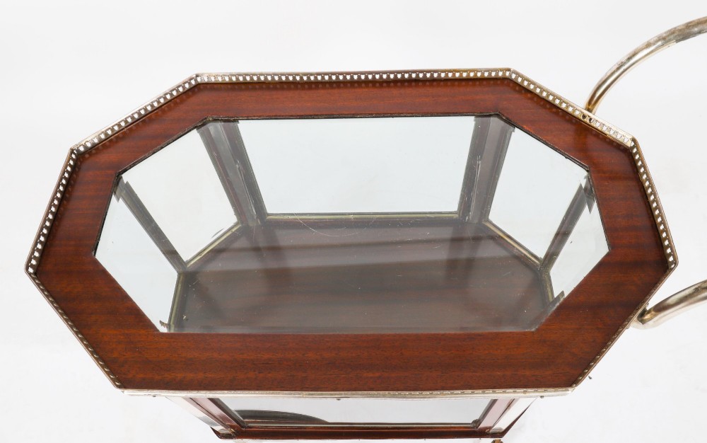 An Art Deco drinks trolley featuring an octagonal glass top with metal gallery trim, wooden side frames, spoked wheels, and a drop-down door. View XI