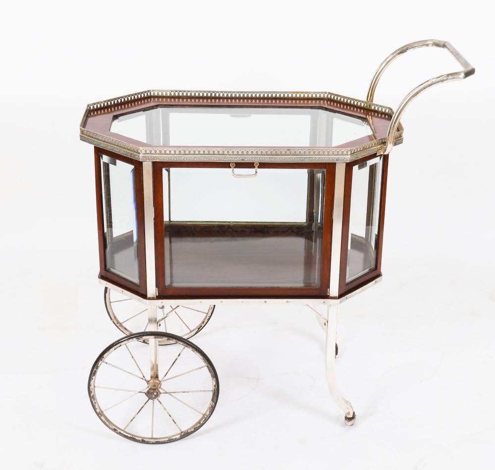 An Art Deco drinks trolley featuring an octagonal glass top with metal gallery trim, wooden side frames, spoked wheels, and a drop-down door. View XII