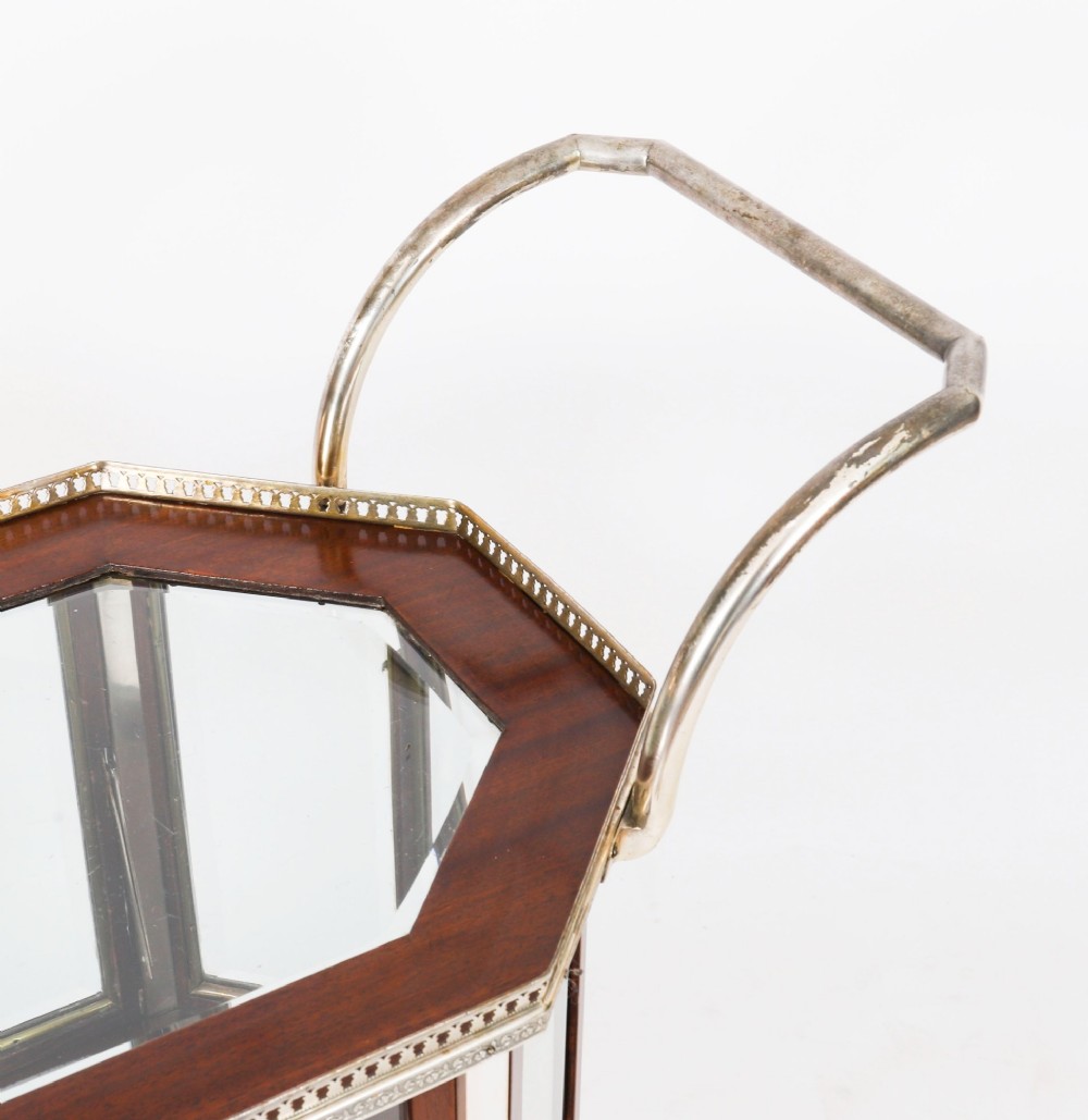An Art Deco drinks trolley featuring an octagonal glass top with metal gallery trim, wooden side frames, spoked wheels, and a drop-down door. View XIII