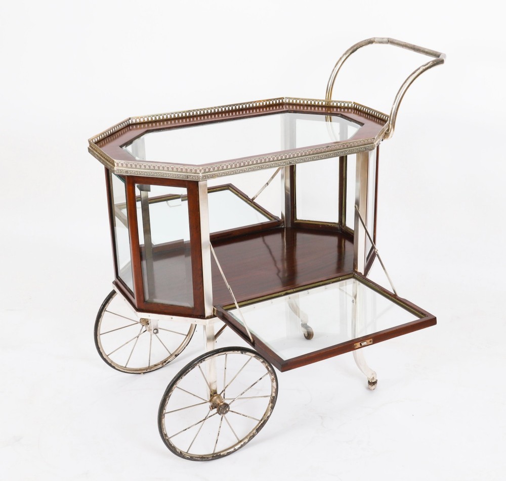 An Art Deco drinks trolley featuring an octagonal glass top with metal gallery trim, wooden side frames, spoked wheels, and a drop-down door. View XIV