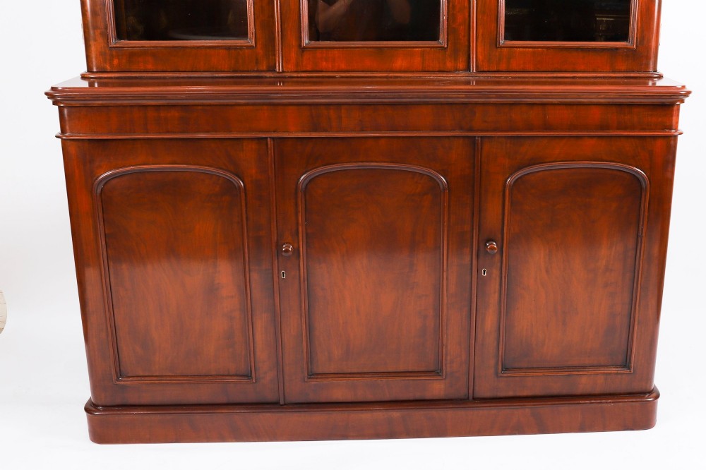 A large 19th-century Victorian flame mahogany library bookcase featuring a glazed three-door upper section filled with books above a solid three-door cupboard base. View V