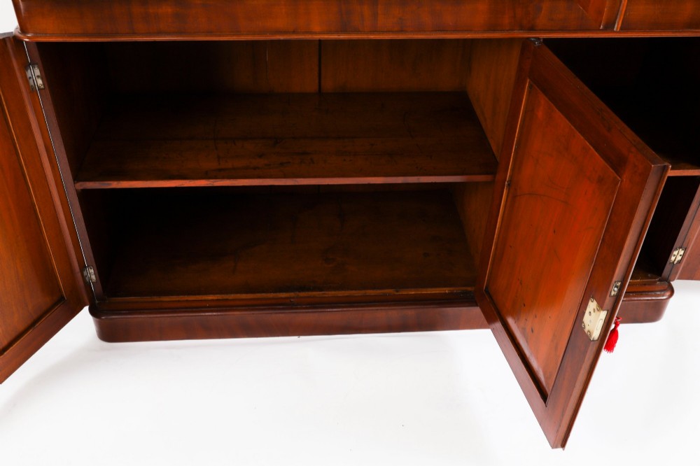 A large 19th-century Victorian flame mahogany library bookcase featuring a glazed three-door upper section filled with books above a solid three-door cupboard base. View XIV