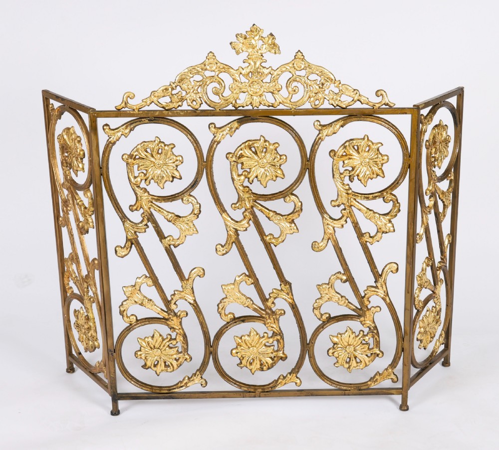 A nineteenth-century French Louis XIV Revival three-panel folding fire screen made from gilt brass featuring intricate floral scrollwork and an ornate cresting motif.