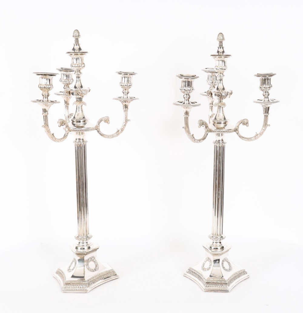A pair of silver-plated four-light candelabra with fluted columns, scroll branches, and laurel wreath detailing on square bases.