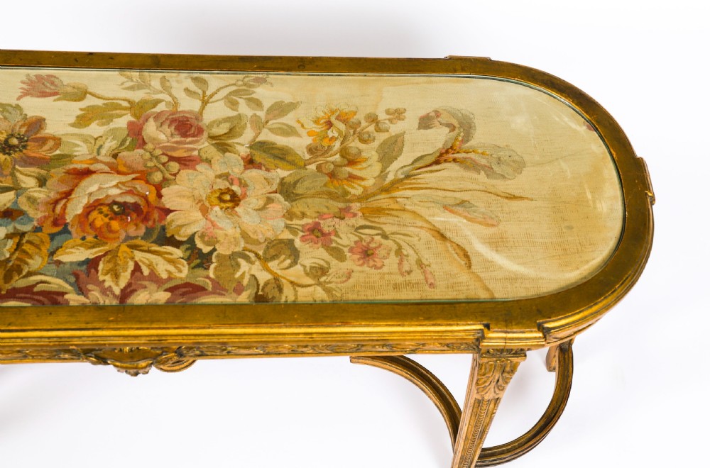 An early 20th-century oval French Louis XVI style giltwood low table featuring an inlaid tapestry top under glass and carved legs connected by a stretcher. View V