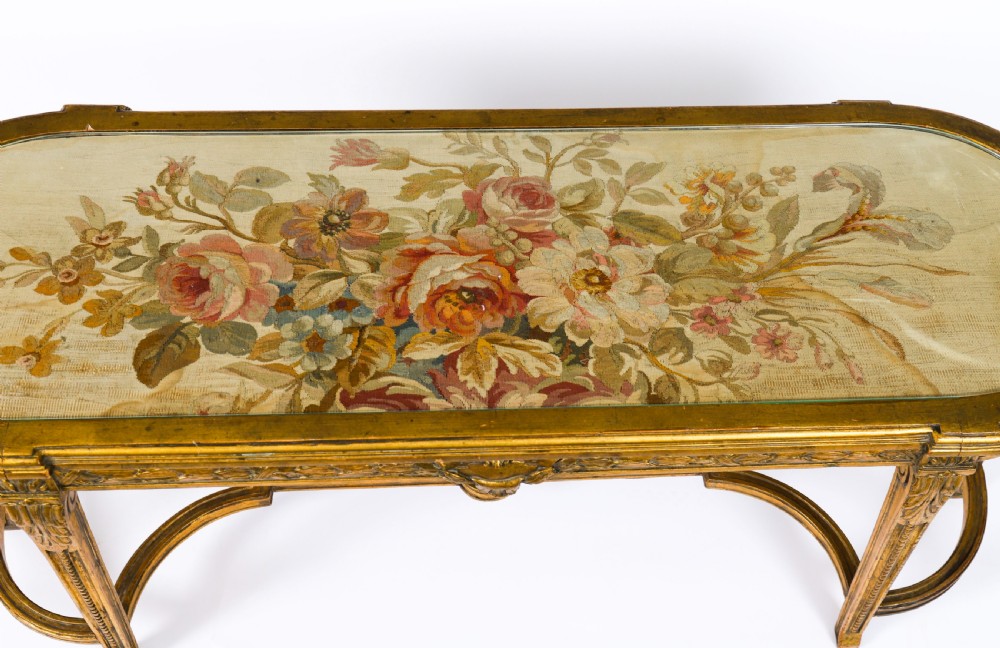 An early 20th-century oval French Louis XVI style giltwood low table featuring an inlaid tapestry top under glass and carved legs connected by a stretcher. View VII