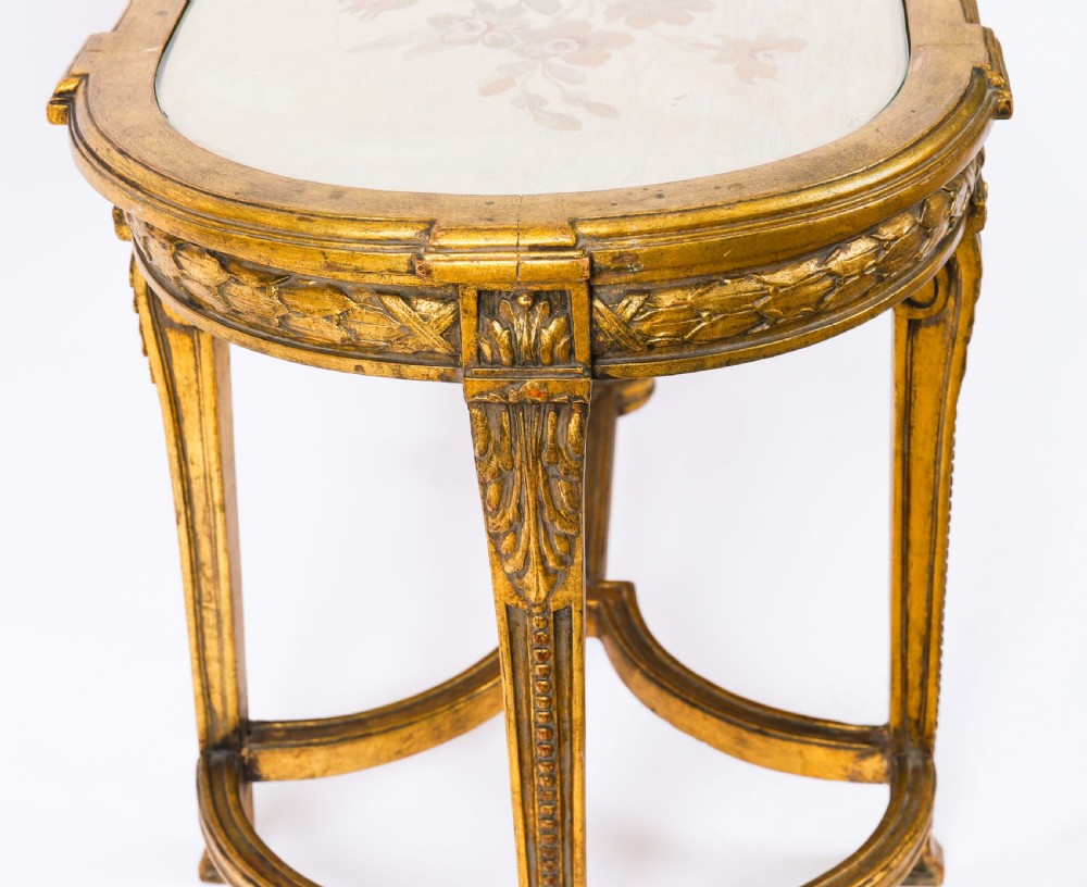 An early 20th-century oval French Louis XVI style giltwood low table featuring an inlaid tapestry top under glass and carved legs connected by a stretcher. View X