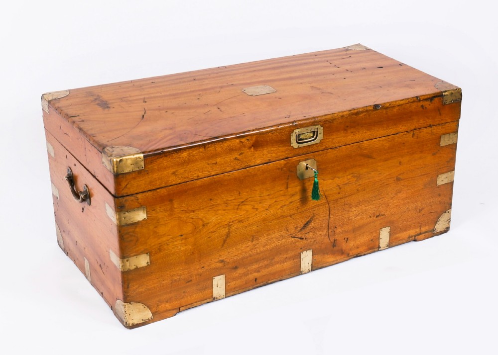 A rectangular 19th-century warm brown camphorwood military campaign trunk featuring flush brass corner brackets, protective metal straps, side drop handles, and a central brass keyhole escutcheon.
