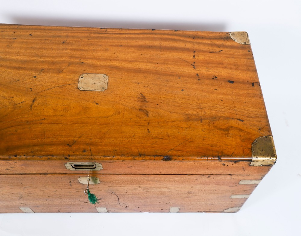 A rectangular 19th-century warm brown camphorwood military campaign trunk featuring flush brass corner brackets, protective metal straps, side drop handles, and a central brass keyhole escutcheon. View VI