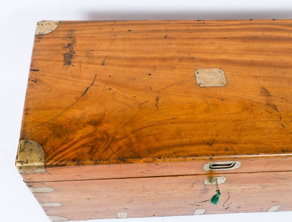 A rectangular 19th-century warm brown camphorwood military campaign trunk featuring flush brass corner brackets, protective metal straps, side drop handles, and a central brass keyhole escutcheon. View VII